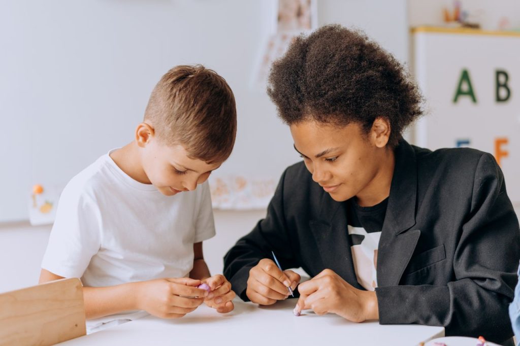 The Art of Drawing Readers In: Your attractive post title goes here A teacher assists a young student with an educational activity in a classroom setting.